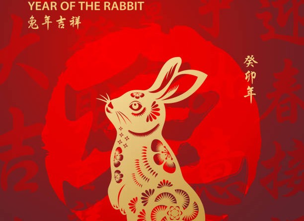 Celebrate the Year of the Rabbit 2023 with gold colored rabbit paper art and red stamp on the red Chinese language background, the background red stamp means rabbit, the horizontal Chinese phrase means wish you luck in the year of the rabbit and the vertical Chinese phrase means Year of the Rabbit according to Chinese lunar calendar system